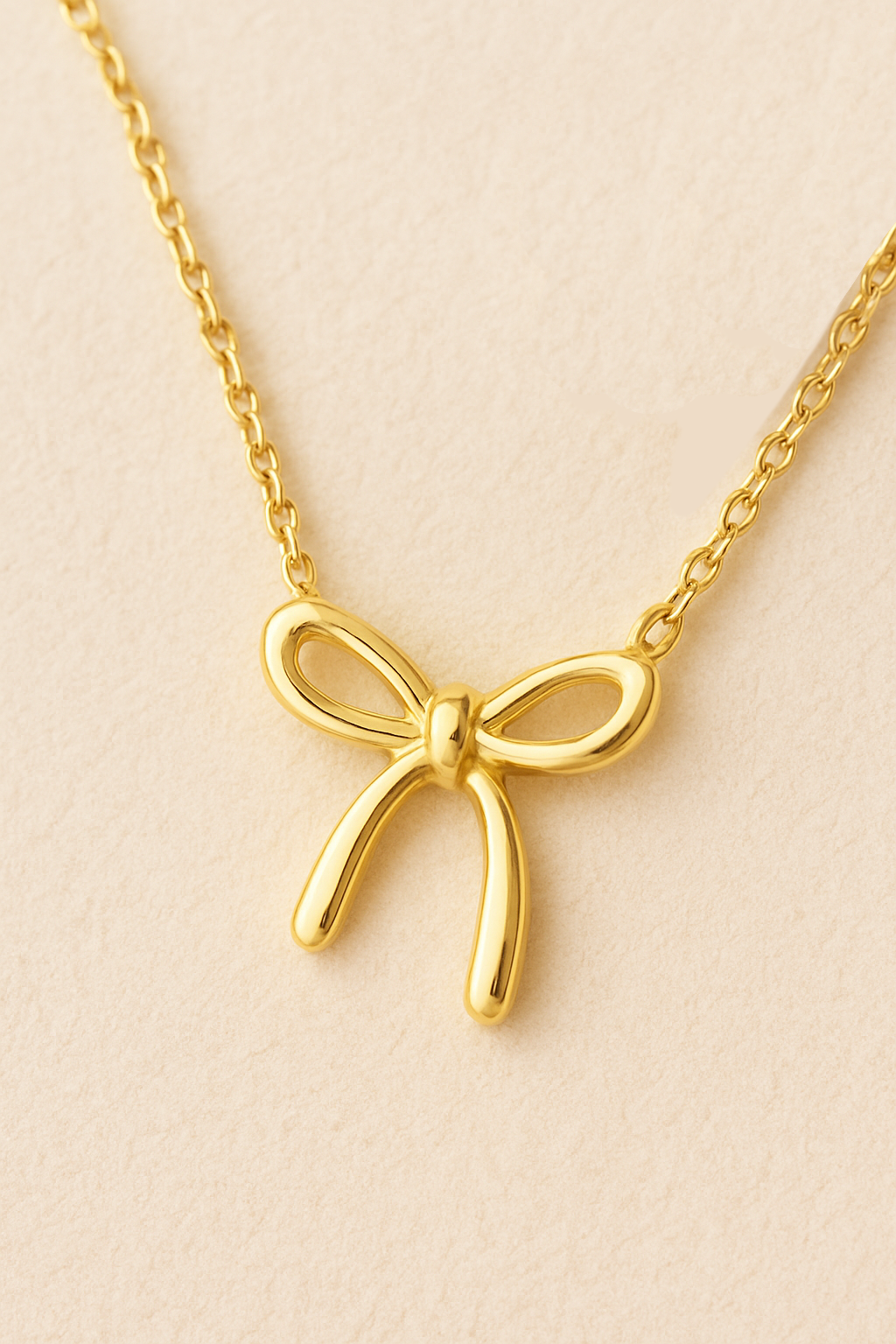 Gold bow necklace on a beige background with scattered pearls close up